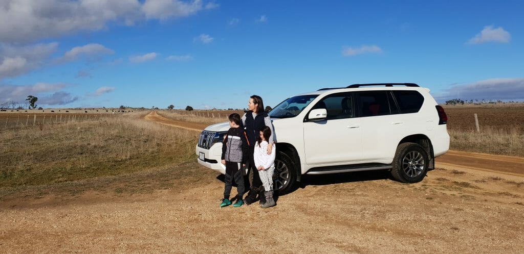 Mum and kids lean on white 4-wheel-drive in Snowy Mountains