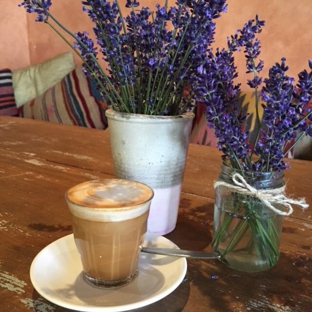 Latte in a clear glass on table with two pots of lavendar