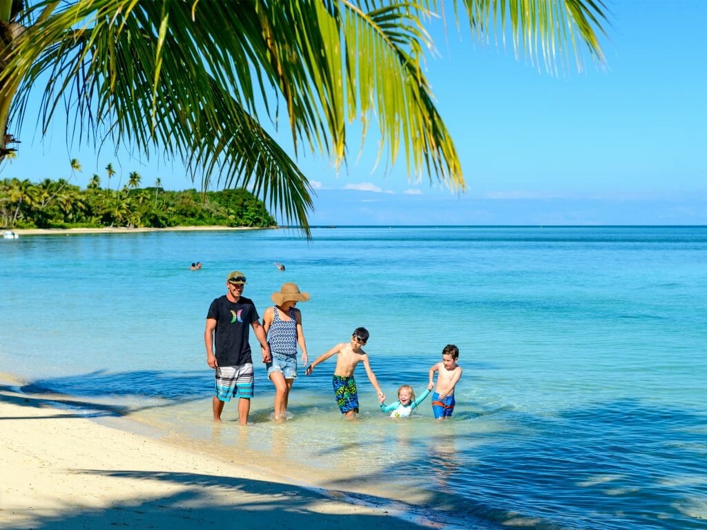 Family of five walk along tropical beach in Fiji