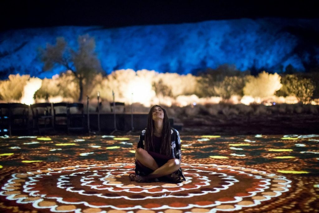 Girl sits on large-scale indigenous artwork at Parrtjima in Alice Springs