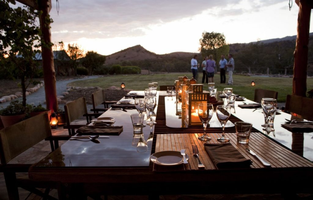 Dinner table set up at sunset with people standing in background drinking wine