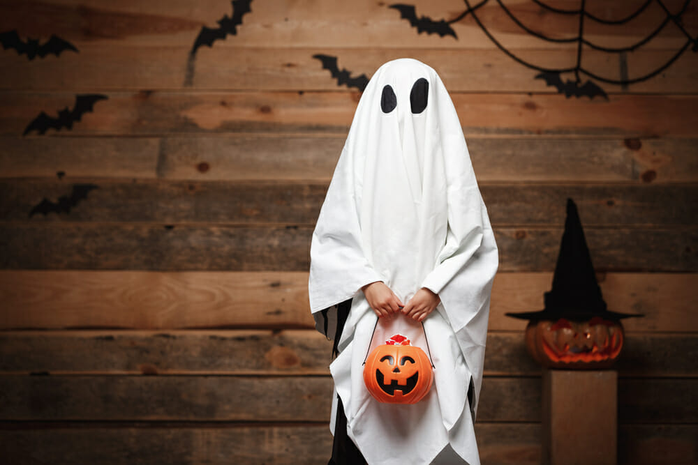 child dressed as a ghost ready to go trick or treating for Halloween