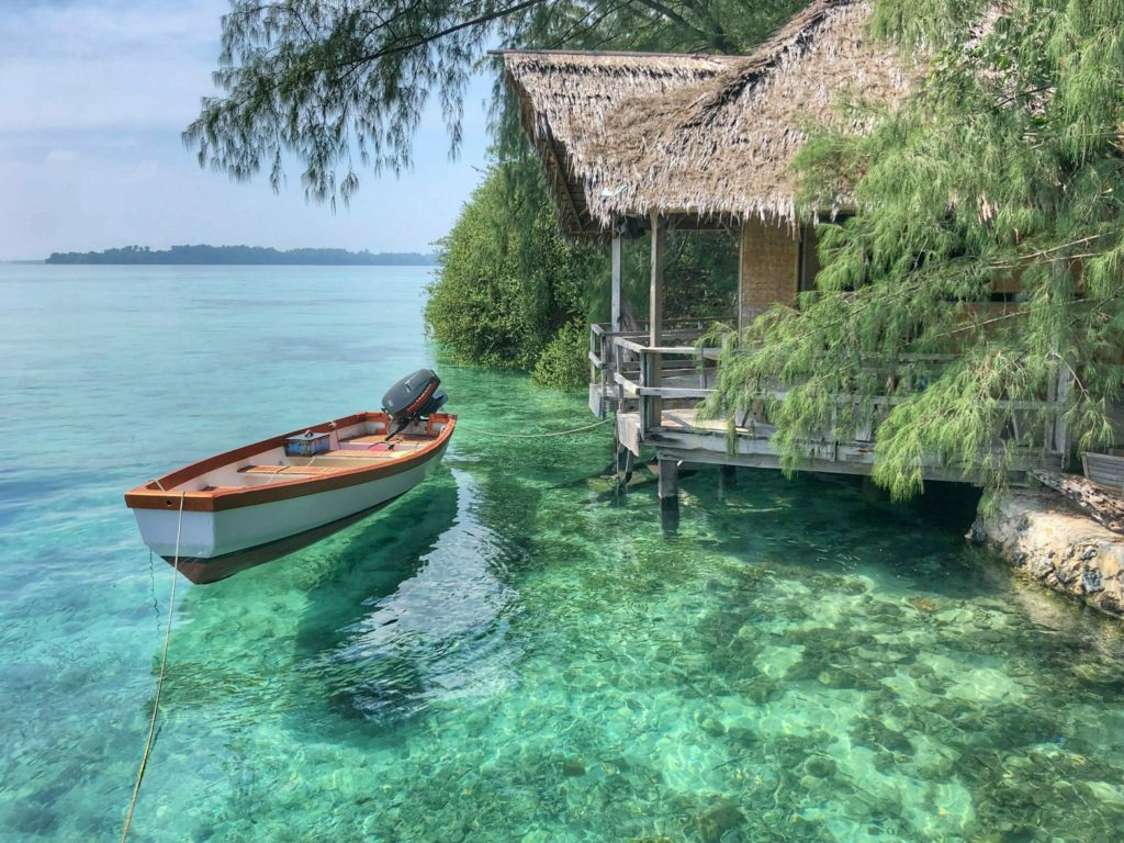 Boat floating in clear water next to bungalow