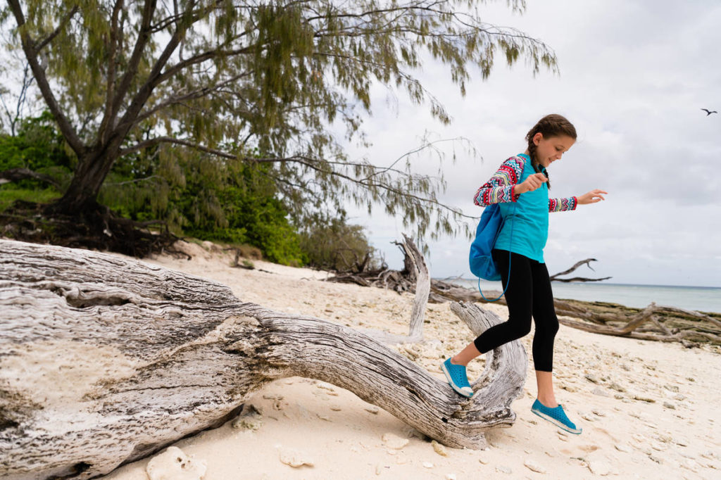 young girl steps over a log on the beach wearing a backpack and trainers on Lady Musgrave Island