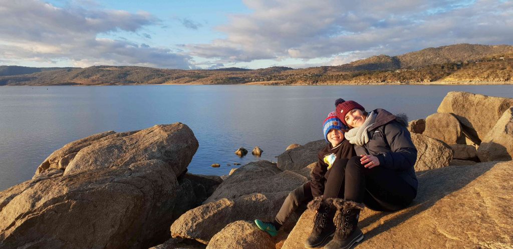 mother and son sitting on the rocks on the edge of Lake Jindabyne at sunset