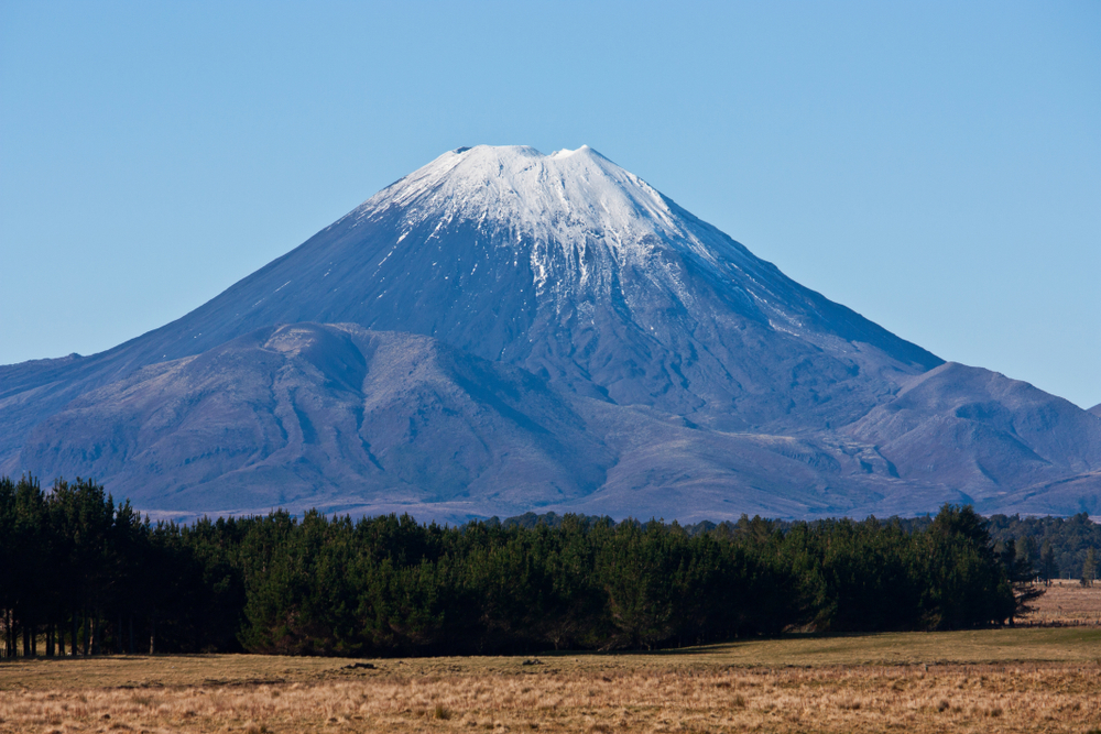 The top of the Mount Doom / Ngauruhoe covered in snow overlooking fields and trees in the North Island in New Zealand