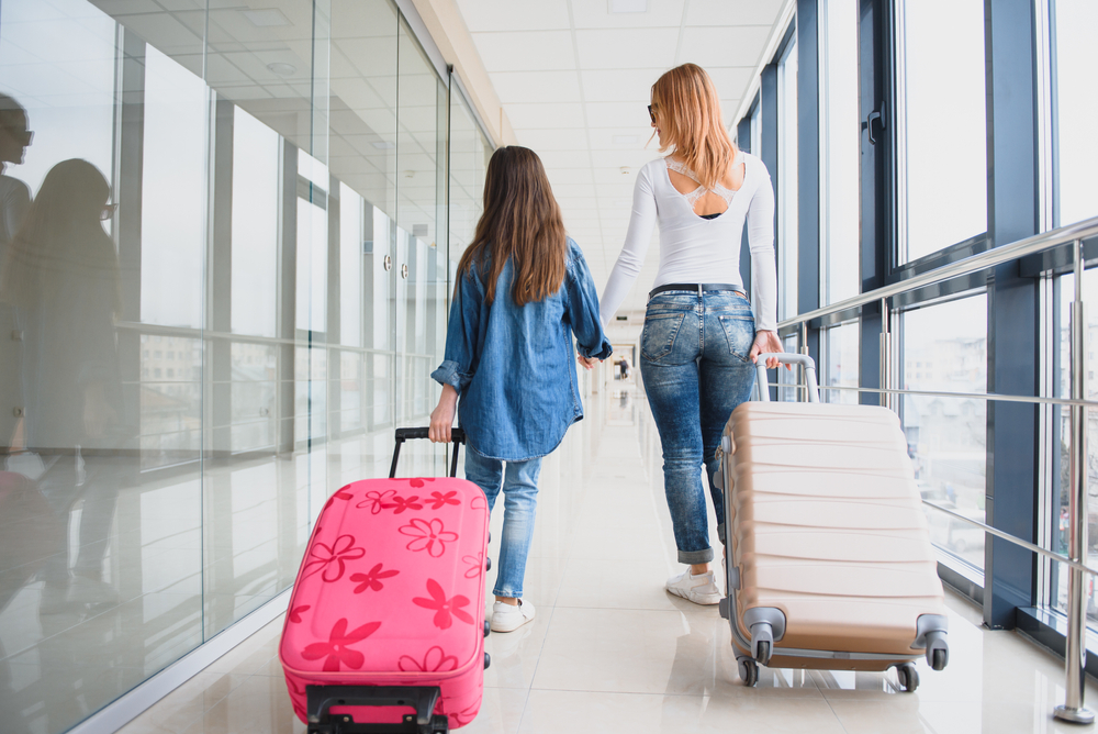 mother and daughter walking through an airport with hand luggage
