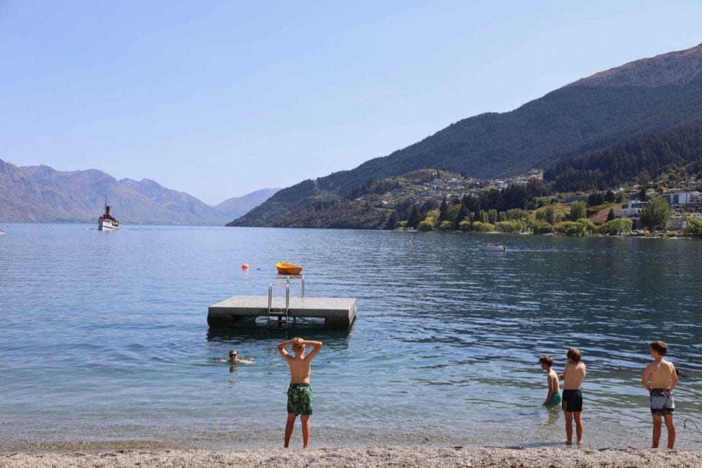 TSS Earnslaw in the background as young boys decide if they want to swim out to the pontoon from Queenstown beach