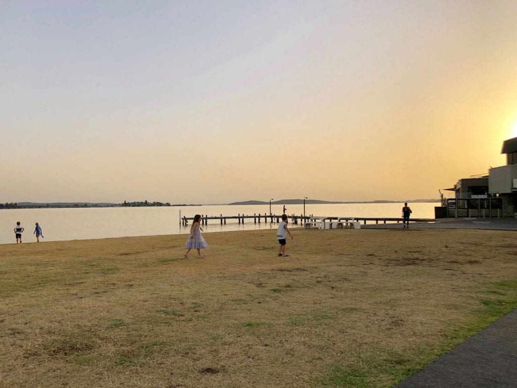 young kids running on the grass as the sun sets over Lake Macquarie