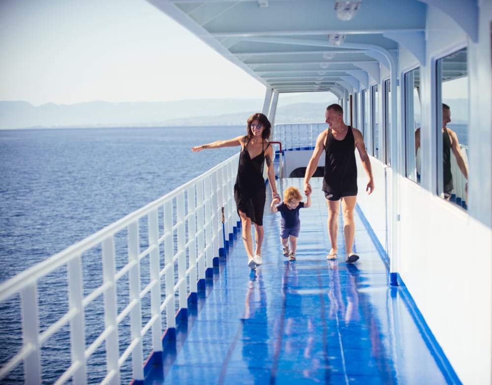 Father, mother and child walk on deck of cruise liner with sea on background.