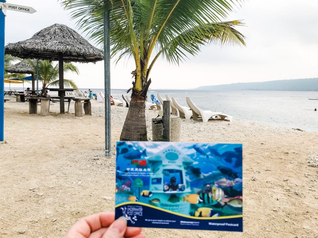 waterproof postcard on the beach with sign pointing to underwater post box in Vanuatu