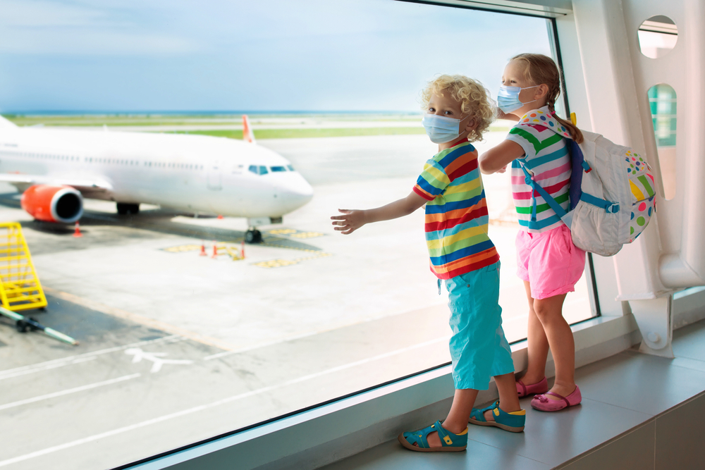 afe travel with young child and baby. Kids boarding airplane in surgical masks.