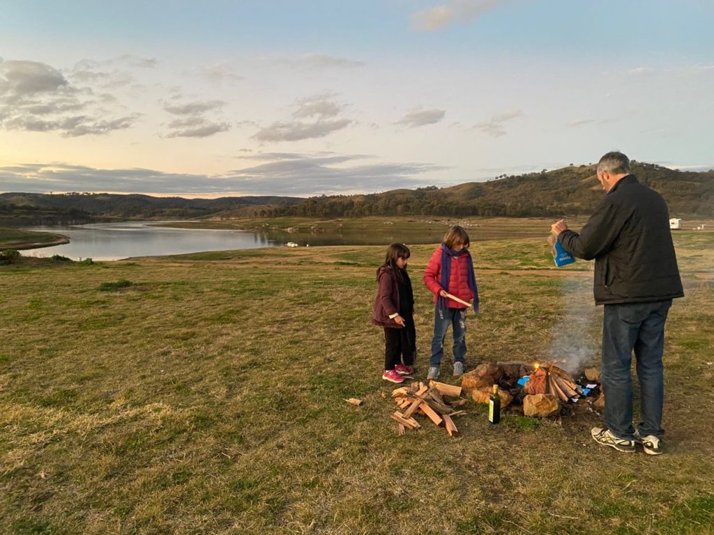 2 kids and a man setting a camp fire in an  open field