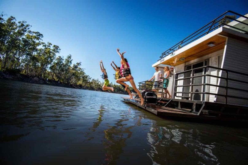 kids jumping off the back of a houseboat in life vests as the parents watch. Part of a houseboat family holiday on the Murray River