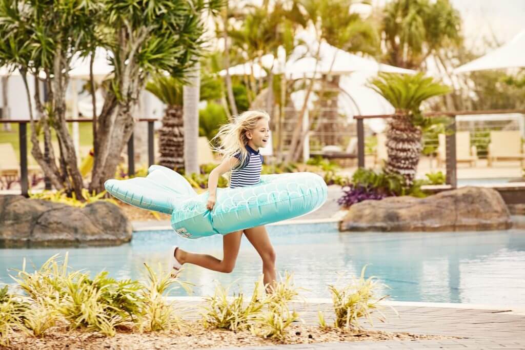 little girl wearing blue floaty ring running beside the hotel pool on Daydream Island
