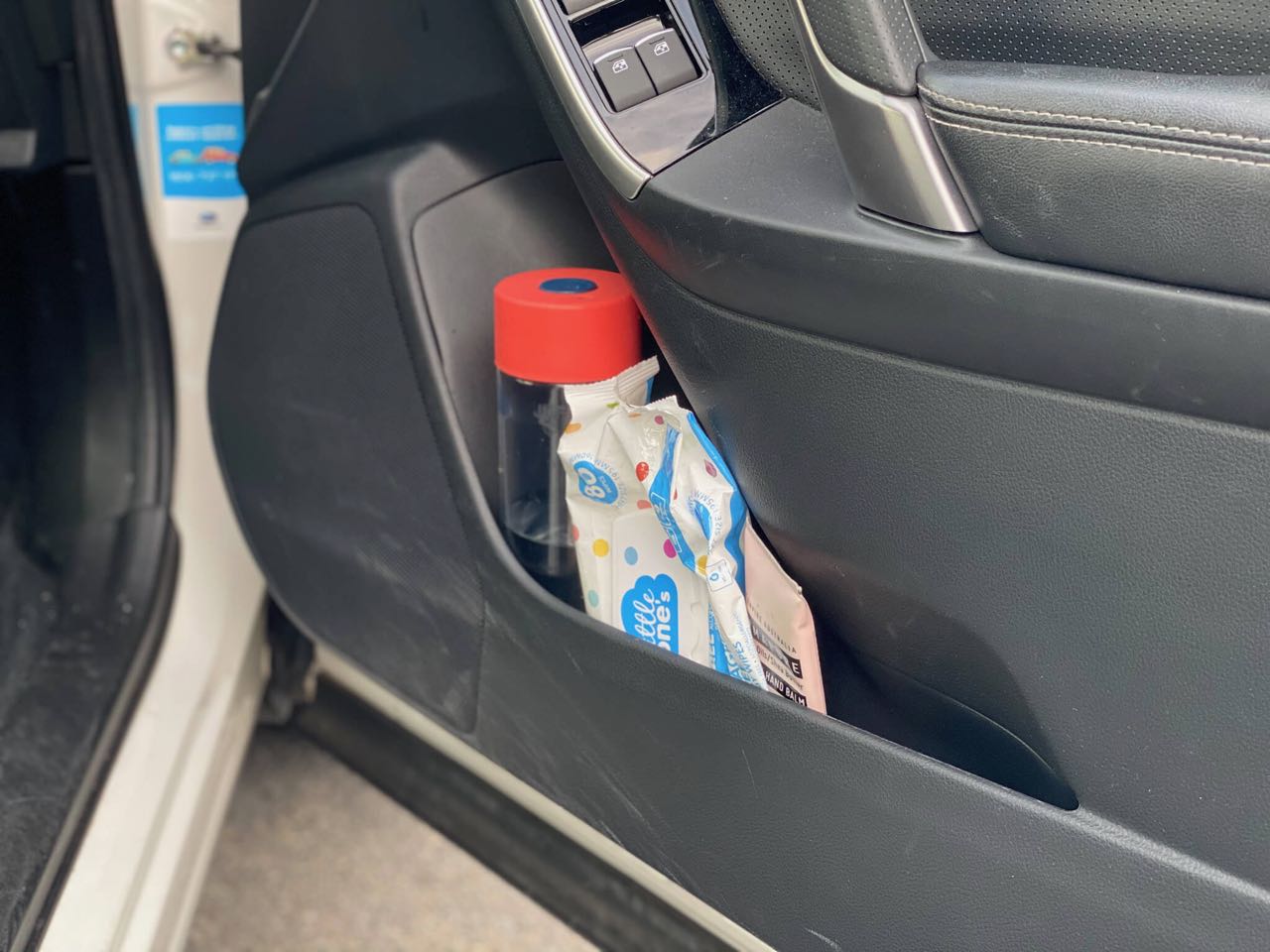 Inside of a car door where there is a water bottle, packet of baby wipes and tube of hand cream in the pocket 