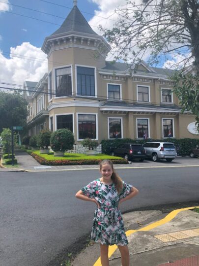 Young girl in a floral dress with her hands on her hips in front of cream and white two story building in San Jose Costa Rica